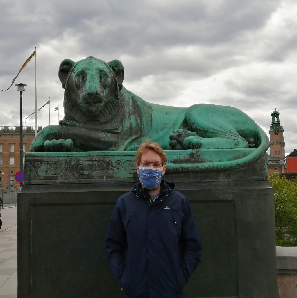 The author's masked partner stands in front of a lion statue in Stockholm